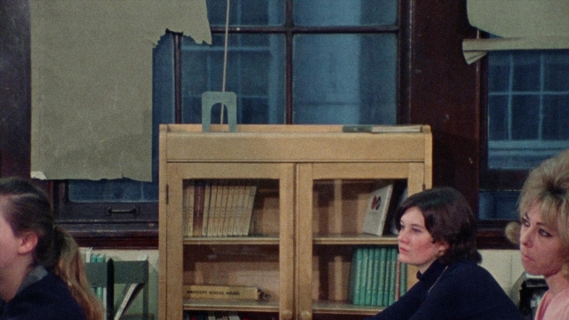 Wide shot frame from Female Trouble — sitting, book, room