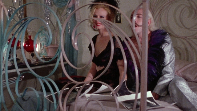 Wide shot frame from Female Trouble — sitting, room, bed