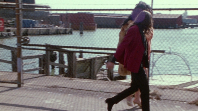 Wide shot frame from Female Trouble — walking, coat, water