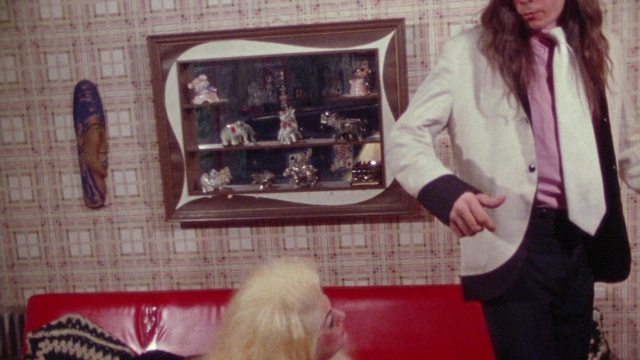 Wide shot frame from Female Trouble — sitting, standing, room