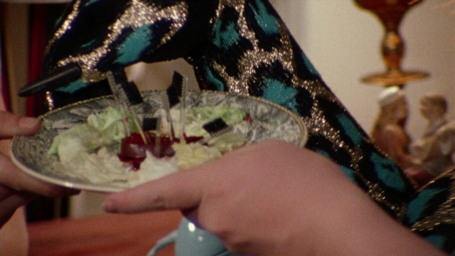 Frame from Female Trouble — standing, plate, table