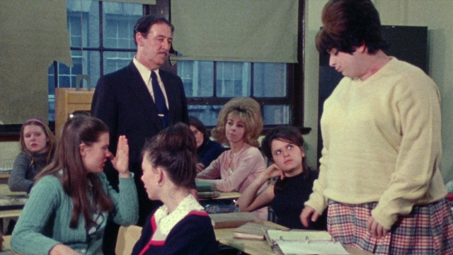Wide shot frame from Female Trouble — sitting, standing, room