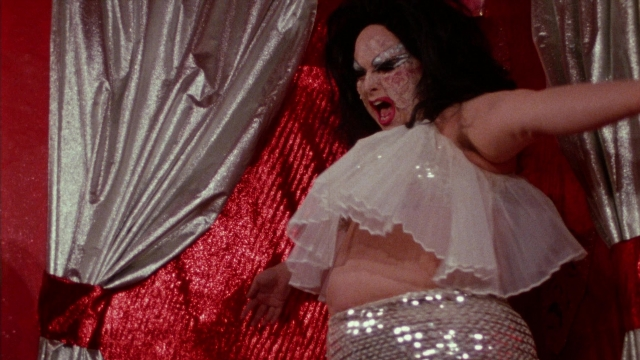 Wide shot frame from Female Trouble — standing, hair, curtain