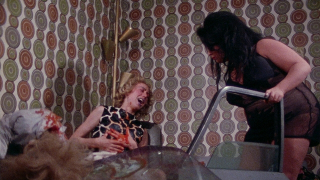 Wide shot frame from Female Trouble — standing, room, hand