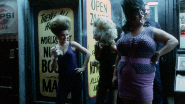 Wide shot frame from Female Trouble — standing, dialogue, dress