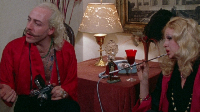 Close-up frame from Female Trouble — sitting, room, table
