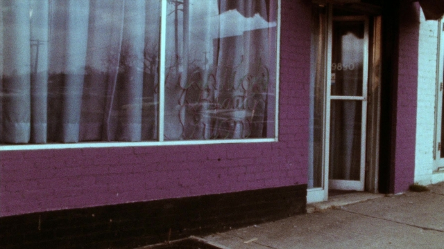 Frame from Female Trouble — table, door, street