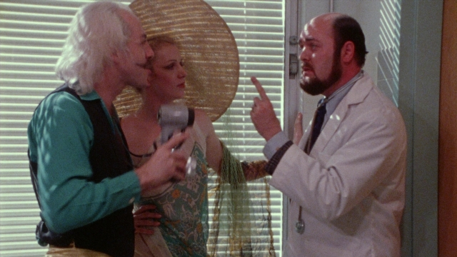 Wide shot frame from Female Trouble — standing, room, dialogue