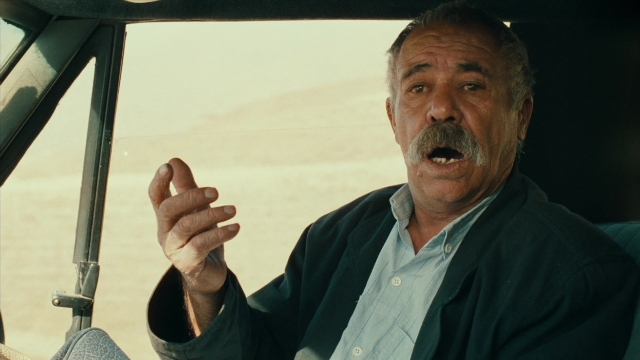 Medium shot frame from Ta'm e guilass — sitting, car, hand