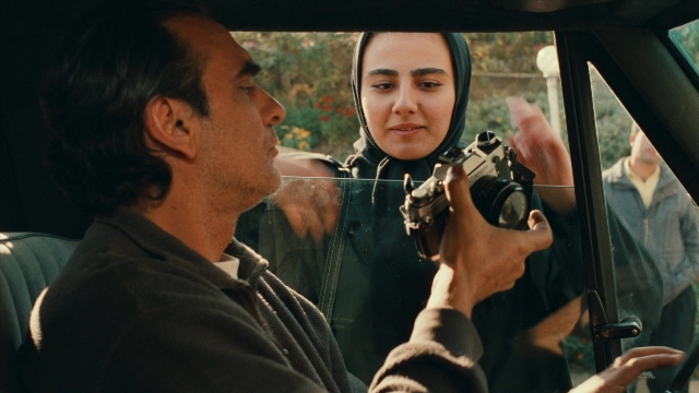 Wide shot frame from Ta'm e guilass — sitting, standing, car