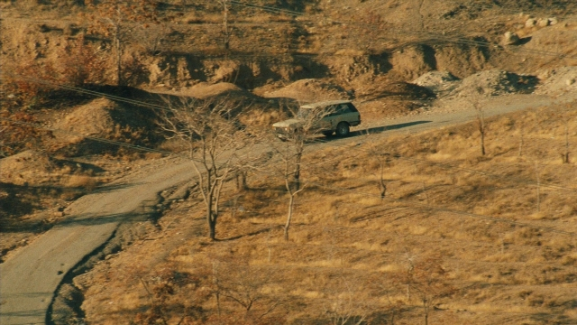 Wide shot frame from Ta'm e guilass — street, car, wheel