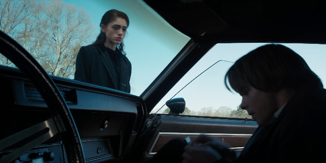 Wide shot frame from Stranger Things — sitting, standing, phone