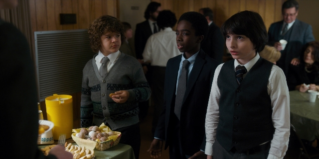 Wide shot frame from Stranger Things — standing, room, table