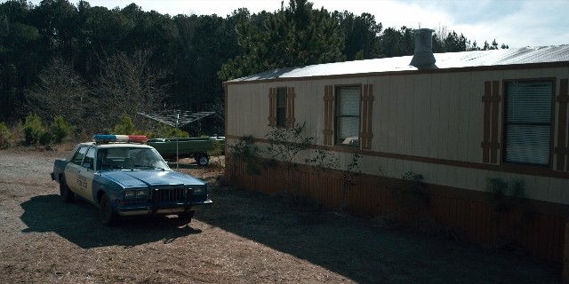Wide shot frame from Stranger Things — car, house, wheel