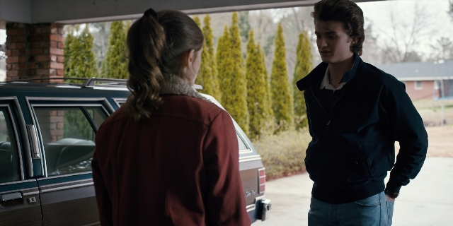 Wide shot frame from Stranger Things — standing, dialogue, car