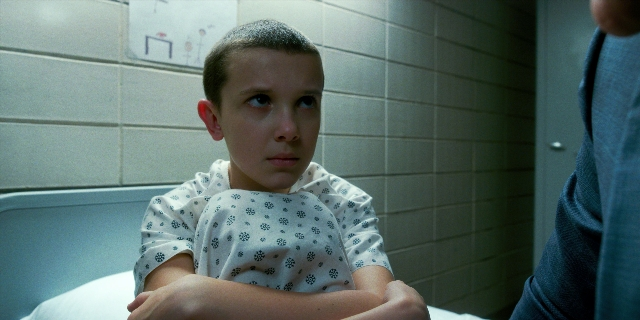 Medium shot frame from Stranger Things — sitting, bed, hand