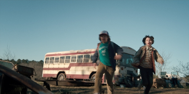 Wide shot frame from Stranger Things — hat, shirt, bus