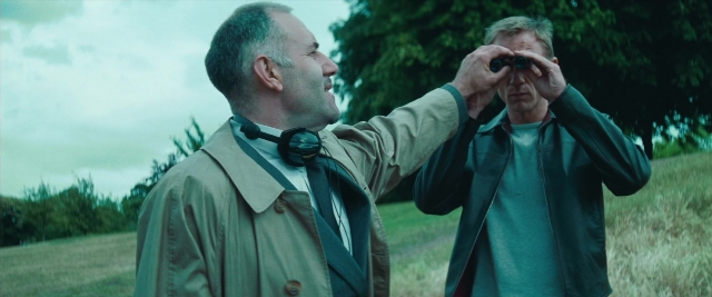 Wide shot frame from Layer Cake — standing, coat, tie