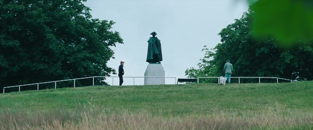 Wide shot frame from Layer Cake — standing, hat, dog