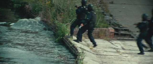 Wide shot frame from Layer Cake — walking, water, gun