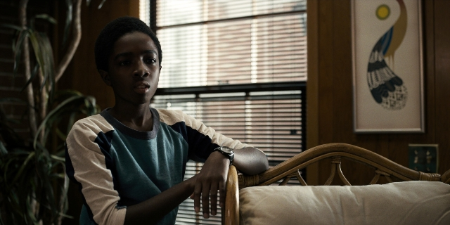 Wide shot frame from Stranger Things — sitting, room, shirt