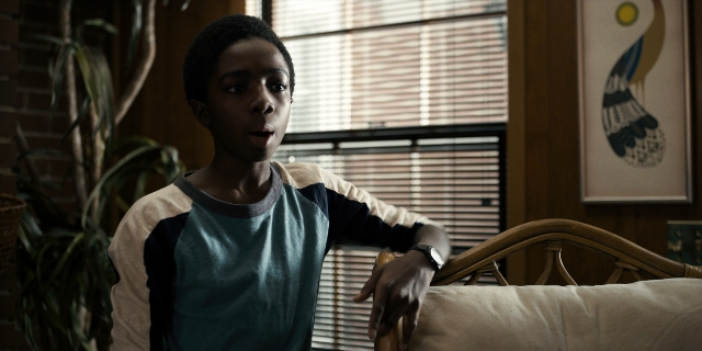 Wide shot frame from Stranger Things — sitting, room, shirt