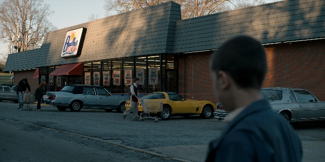 Wide shot frame from Stranger Things — walking, street, car