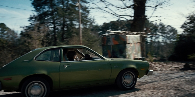 Wide shot frame from Stranger Things — door, street, car