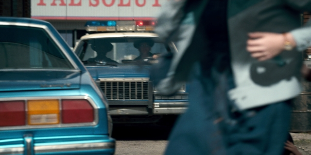 Wide shot frame from Stranger Things — street, car, bag