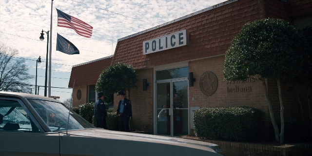 Wide shot frame from Stranger Things — standing, uniform, flag