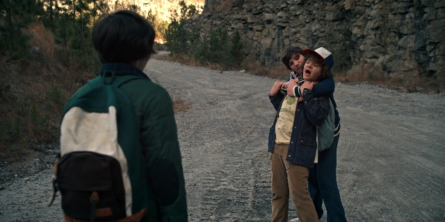 Wide shot frame from Stranger Things — standing, street, hat