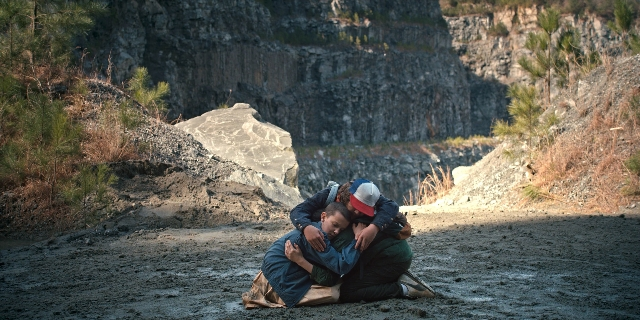 Wide shot frame from Stranger Things — sitting, hat, hug