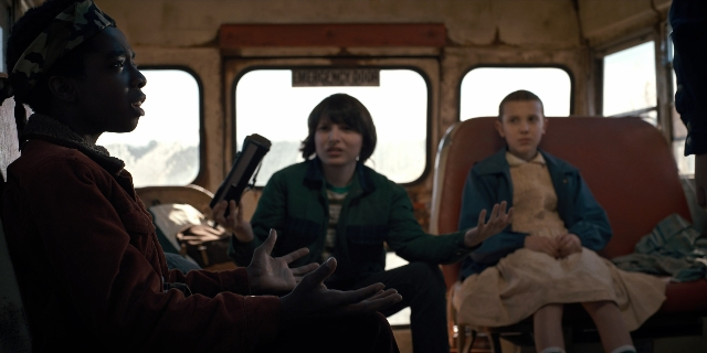 Wide shot frame from Stranger Things — sitting, book, shirt