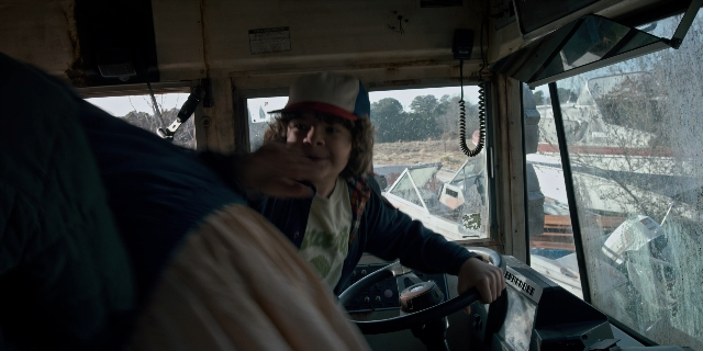 Wide shot frame from Stranger Things — sitting, hat, bus