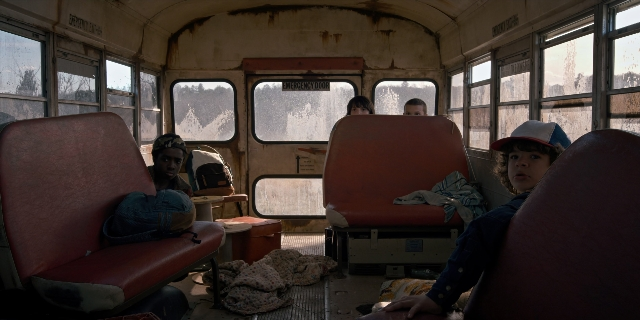 Wide shot frame from Stranger Things — sitting, hat, car