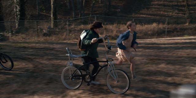 Wide shot frame from Stranger Things — street, bicycle, backpack