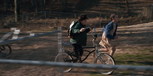 Wide shot frame from Stranger Things — bicycle, backpack, person