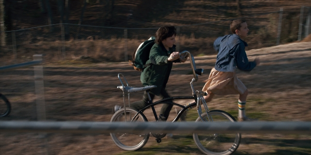 Wide shot frame from Stranger Things — street, bicycle, backpack