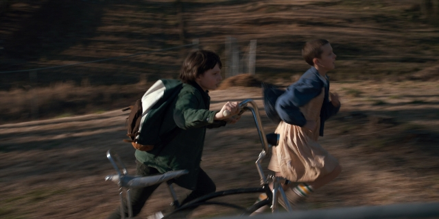 Wide shot frame from Stranger Things — street, bicycle, backpack