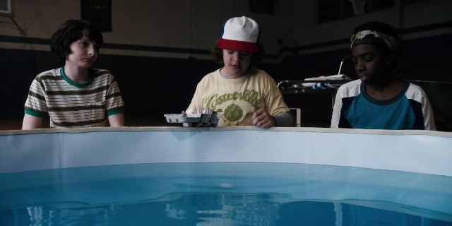 Wide shot frame from Stranger Things — sitting, table, hat