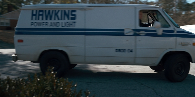 Wide shot frame from Stranger Things — plate, street, van