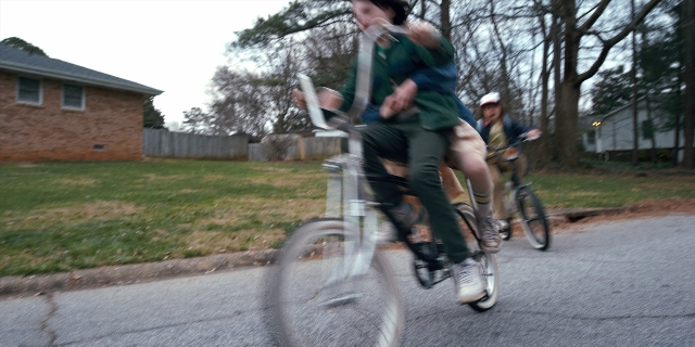 Wide shot frame from Stranger Things — street, hat, bicycle