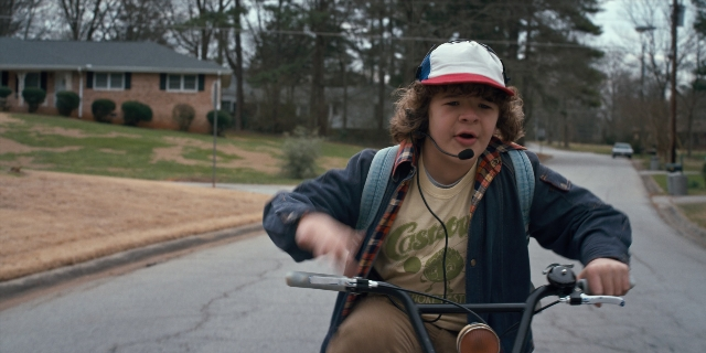 Wide shot frame from Stranger Things — street, hat, bicycle