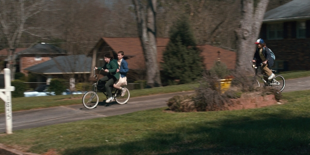 Wide shot frame from Stranger Things — street, hat, bicycle