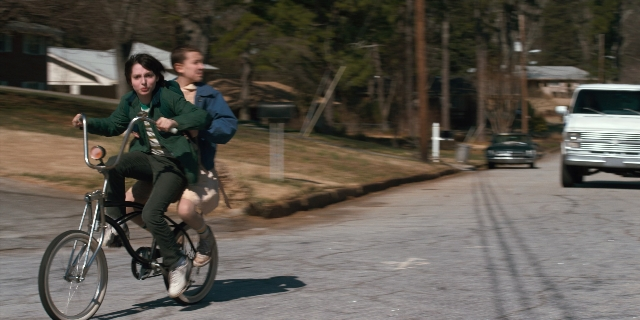 Wide shot frame from Stranger Things — street, car, hand