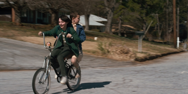 Wide shot frame from Stranger Things — street, bicycle, face