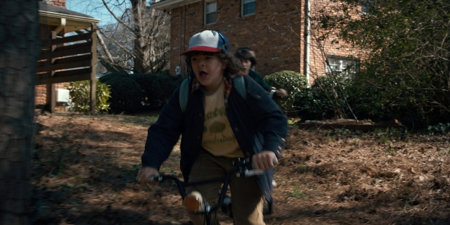 Wide shot frame from Stranger Things — hat, bicycle, shirt
