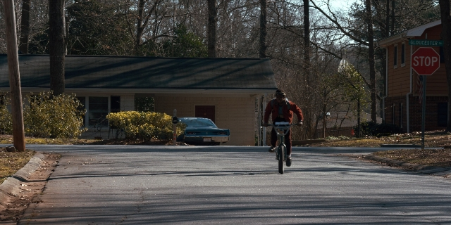 Wide shot frame from Stranger Things — street, hat, car