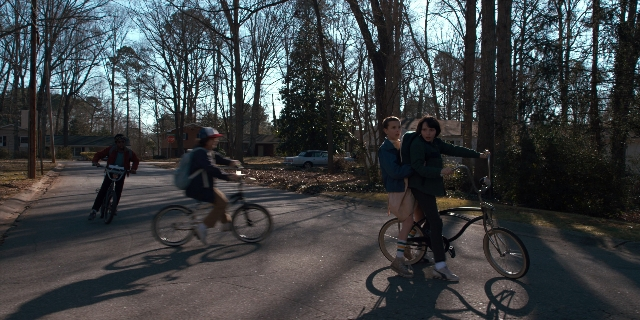 Wide shot frame from Stranger Things — street, hat, bicycle