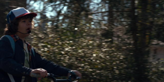 Wide shot frame from Stranger Things — dialogue, hat, bicycle